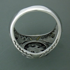 May include: Silver ring with a detailed design on the band and a textured center. The ring is shown from the inside.