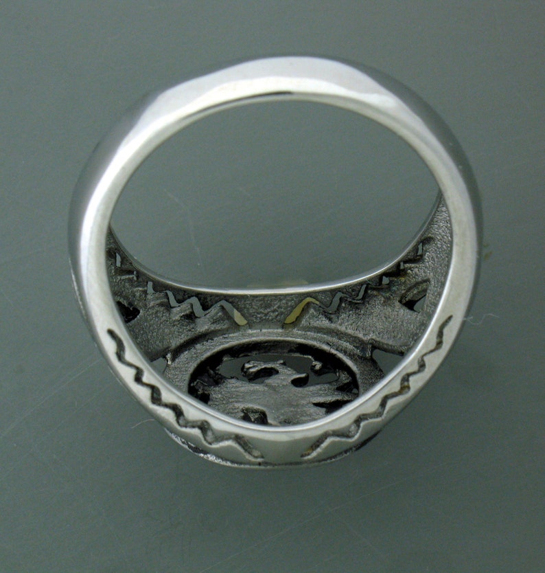 May include: Silver ring with a detailed design on the band and a textured center. The ring is shown from the inside.