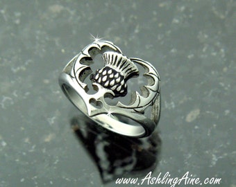 May include: A silver ring with a heart-shaped design featuring a stylized thistle flower.
