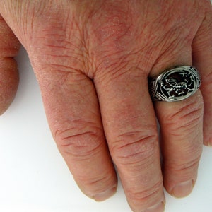 May include: A silver ring with a detailed design of a dragon on the top. The ring is worn on the middle finger of a hand.