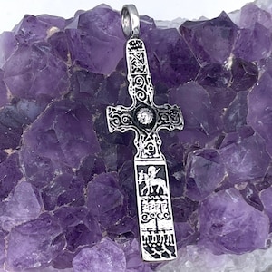 May include: A silver Celtic cross pendant with intricate details and a black enamel finish. The cross features a small, round, white stone in the center and a depiction of a rider on horseback on the lower portion.