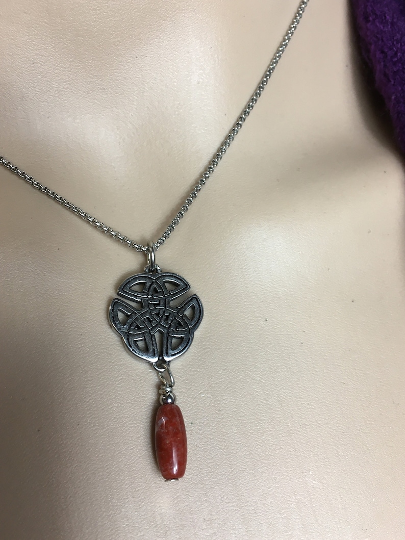 May include: A silver chain necklace with a Celtic knot pendant and a red stone bead.