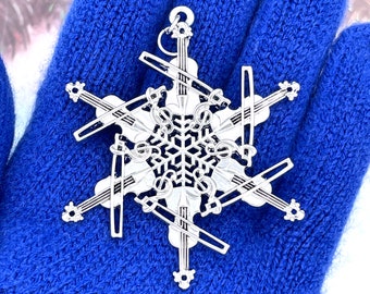 May include: A silver snowflake ornament with six violin-shaped arms. The ornament is decorated with musical notes and a snowflake design in the center.