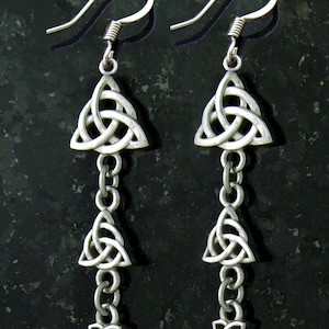 May include: Silver dangle earrings with three Celtic knot charms. Each charm is a triangular knot with a smooth, polished finish.