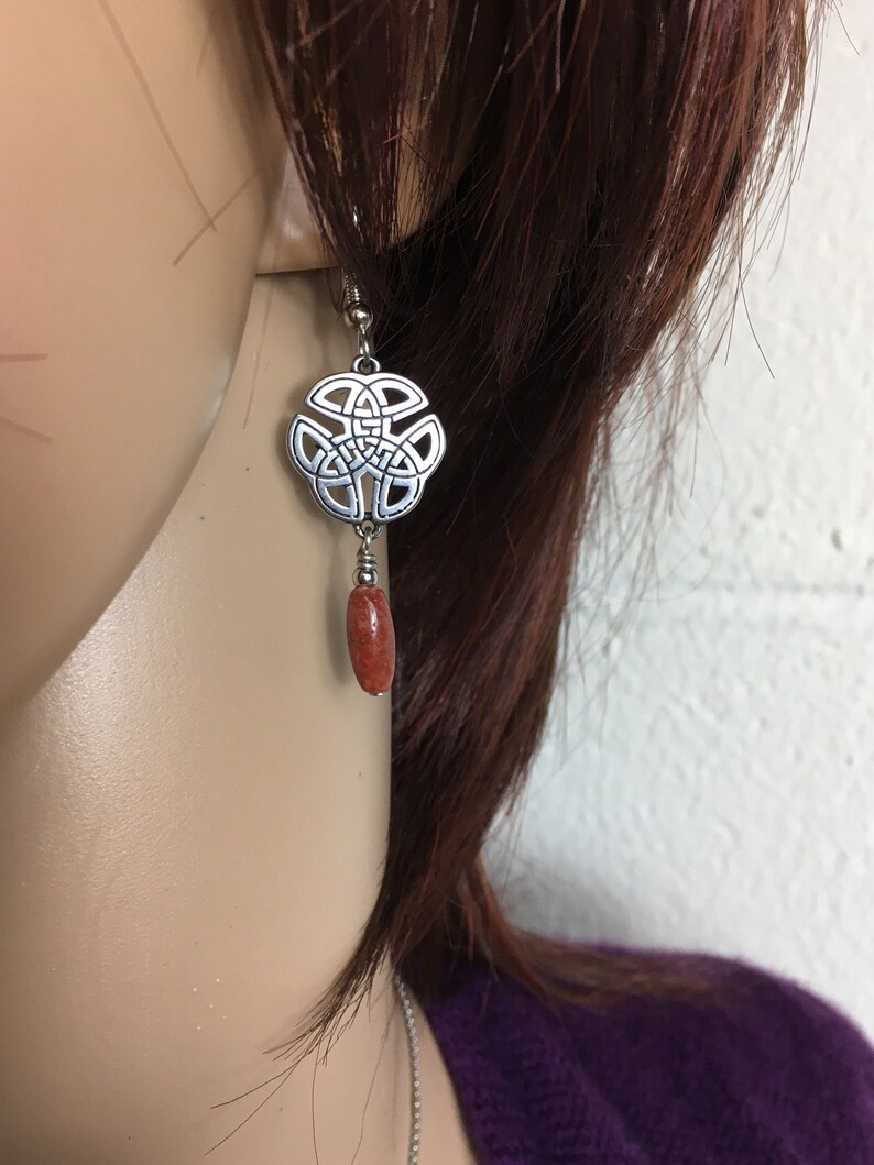 May include: Silver Celtic knot earrings with a dangling red coral bead.