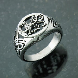 May include: A silver ring with a Celtic knot design and a dragon in a circle in the center.