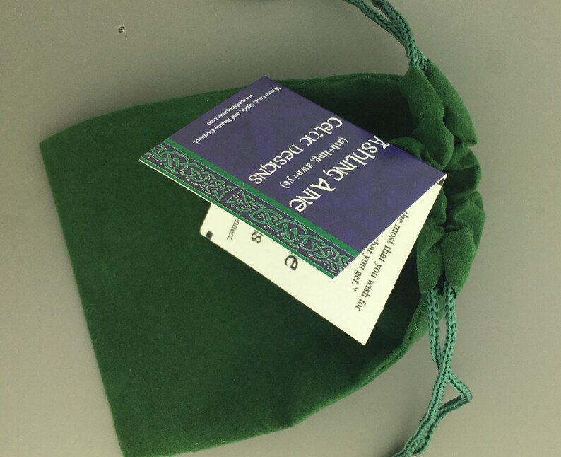 May include: A green velvet drawstring bag with a blue and white card inside. The card has the text "Ashing Aine (ash+ling, awn+ye) Celtic Designs" and a quote: "the most that you wish for that you get."