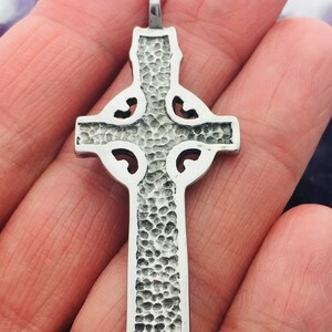 May include: Silver Celtic cross pendant with a hammered texture and intricate knotwork design. The back of the pendant is stamped with "Sterling Silver 925".