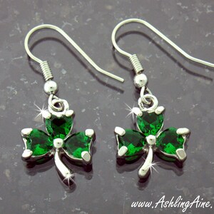 May include: Silver earrings with green shamrock charms. The shamrocks are made of sparkling green crystals.