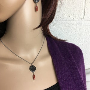May include: A silver necklace and earrings with a Celtic knot design and a red stone pendant.