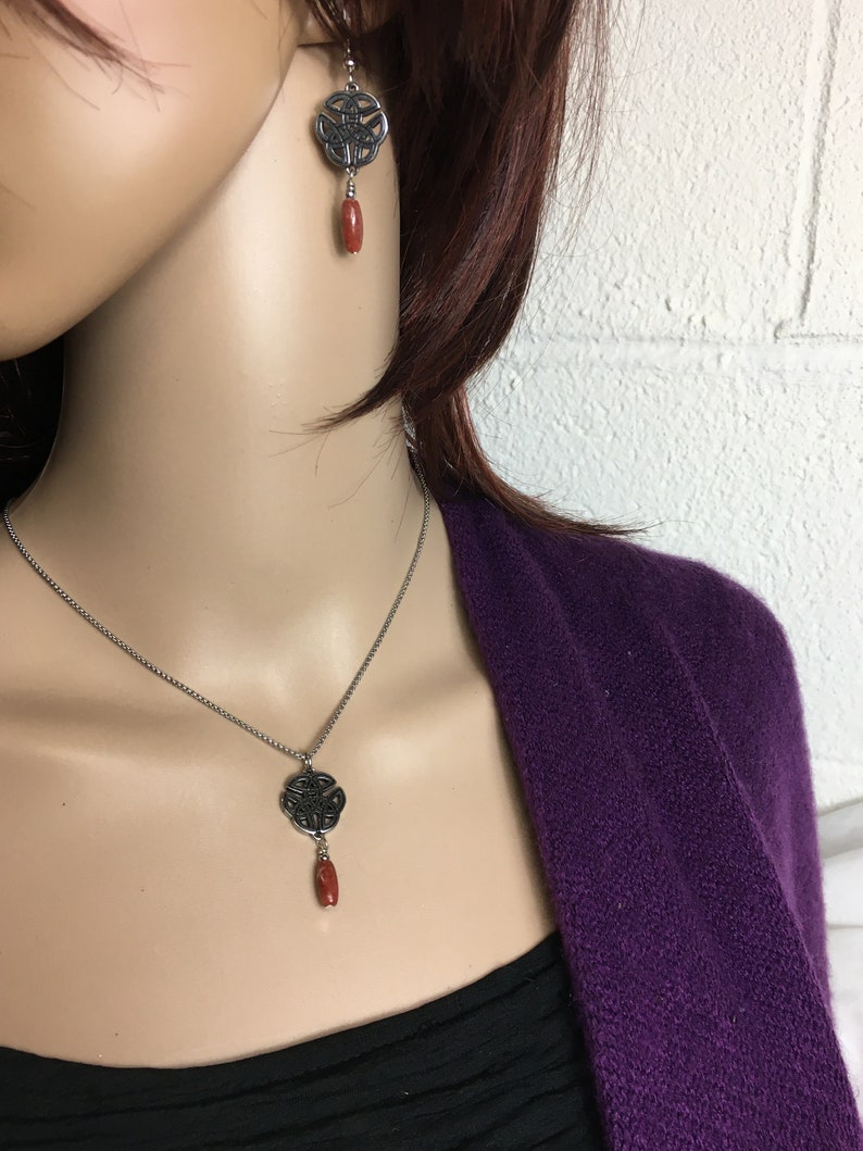 May include: A silver necklace and earrings with a Celtic knot design and a red stone pendant.