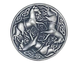 May include: A round, silver-colored metal button or pendant featuring a Celtic knot design. The design includes four stylized horses or animals intertwined with intricate knotwork. The button is set against a white background.