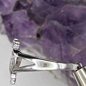 K&ouml;nnte beinhalten: Silberring mit einem detaillierten Design. Der Ring liegt auf einem violetten Hintergrund.