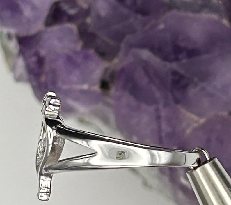 K&ouml;nnte beinhalten: Silberring mit einem detaillierten Design. Der Ring liegt auf einem violetten Hintergrund.