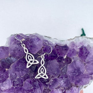 May include: Silver Celtic knot earrings on a bed of amethyst crystals.