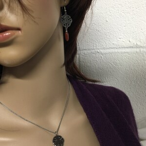 May include: A silver Celtic knot pendant necklace with a red stone accent. Matching earrings with a silver Celtic knot and red stone dangle.