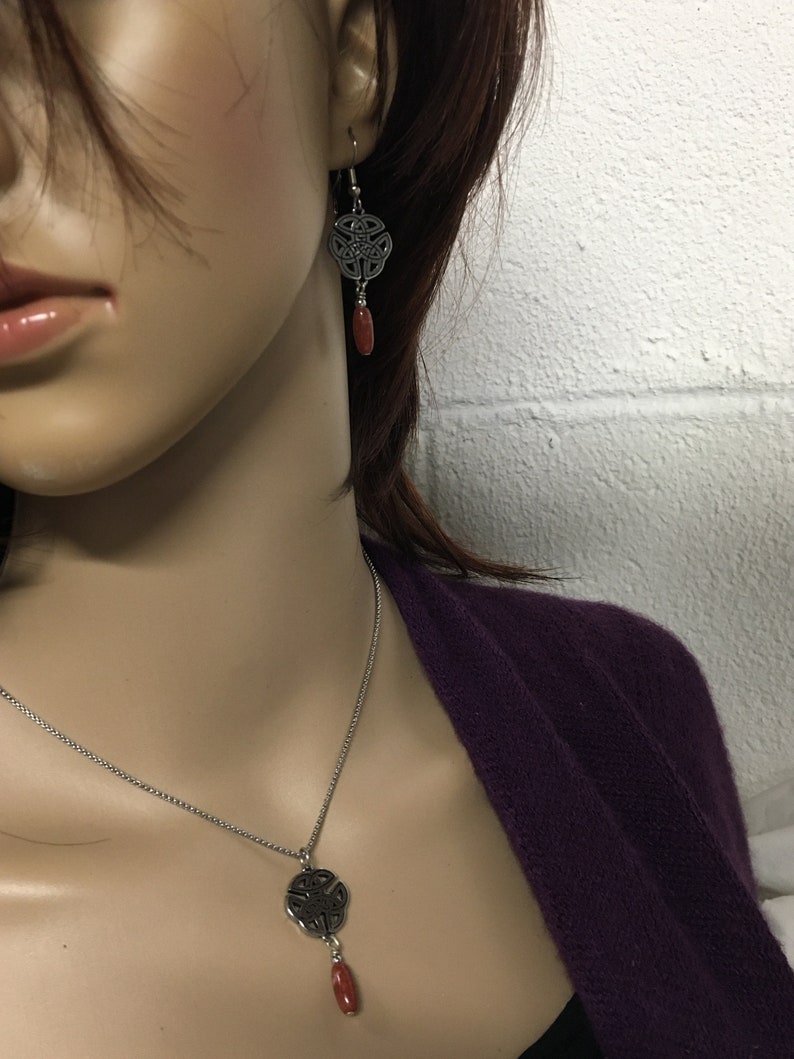 May include: A silver Celtic knot pendant necklace with a red stone accent. Matching earrings with a silver Celtic knot and red stone dangle.