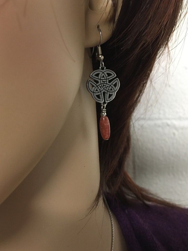 May include: Silver Celtic knot earrings with a dangling orange stone.