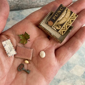 May include: A miniature collection of items including a small box with the text "Punch Hand Made", a small envelope, a pink velvet box, a small key, a small white bead, and a small green leaf.