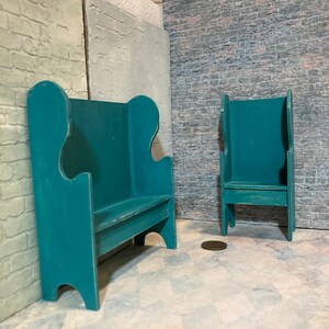 May include: Two teal blue wooden chairs with high backs and a simple design. The chairs are in a room with a brick wall and a tiled floor.