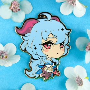 May include: A blue and pink enamel pin featuring a cartoon character with long blue hair, pink horns, and a gold outline. The character is wearing a white and gold outfit and has a pink blush on their cheeks.