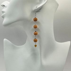 May include: Long brown wooden bead earrings with a small yellow bead at the bottom.