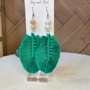 Può includere: Orecchini a forma di piuma in macramè verde con perline color crema e beige. Gli orecchini sono esposti su un'etichetta bianca con la scritta "Lily and Beck".