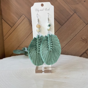 May include: A pair of green tassel earrings with agate beads. The earrings are on a white display stand with the text "Lily and Beck" on a white card behind them.