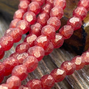 Puede incluir: Primer plano de hebras de cuentas de piedras preciosas facetadas de color rojo anaranjado. Las cuentas tienen un acabado mate texturizado y están ensartadas. La imagen resalta el color y la forma de las cuentas, lo que sugiere su uso en la fabricación de joyas o artesanías.