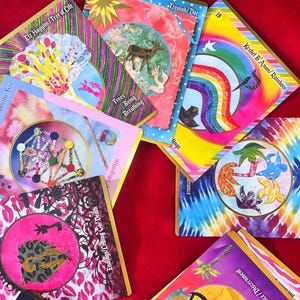 May include: A collection of colorful tarot cards with various illustrations and text. The cards feature images of trees, rainbows, and abstract designs. The text includes phrases like "Tree of Life" and "Rainbow".