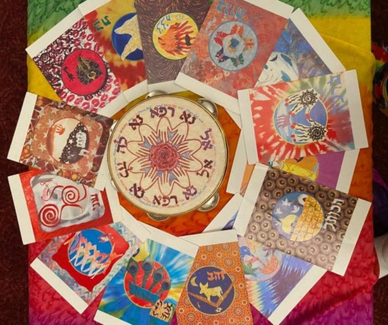 May include: A tambourine surrounded by colorful, tie-dye style cards with various circular designs. The tambourine has text in a circular pattern around a central floral design. The cards feature images of hands, animals, and other symbols.