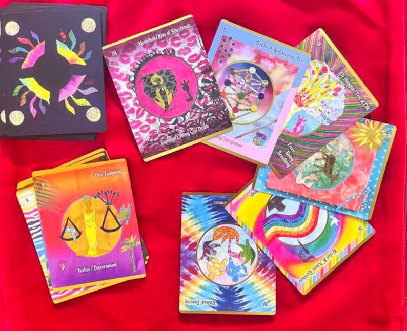 May include: A collection of colorful oracle cards with various illustrations and text. The cards feature images of scales, rainbows, and abstract designs. The cards are arranged on a red surface.