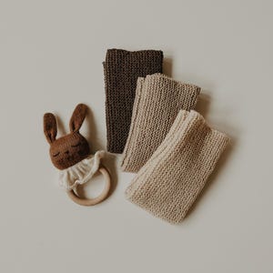 Può includere: Tre coperte per neonati in maglia di colore marrone e beige, con un giocattolo sonaglio a forma di coniglio marrone.