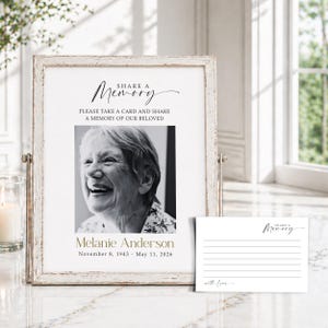 May include: A framed memorial sign with the text "Share a Memory" and a black and white photo of a smiling woman. The sign includes the name "Melanie Anderson" and dates. A small card with lines and the words "with love" is next to the frame.