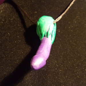 May include: A purple and green eggplant-shaped pendant necklace. The pendant is made of polymer clay and has a green leafy top.
