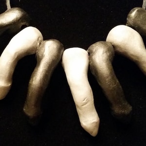 Könnte beinhalten: Eine Halskette aus schwarzen und weißen Keramikperlen in Fingerform. Die Perlen sind auf einer schwarzen Schnur aufgefädelt.