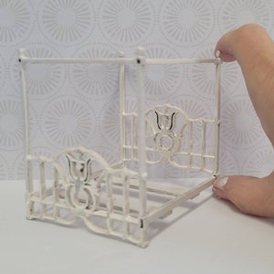 Puede incluir: Marco de cama de metal blanco para casa de mu&ntilde;ecas con dosel y detalles florales decorativos.