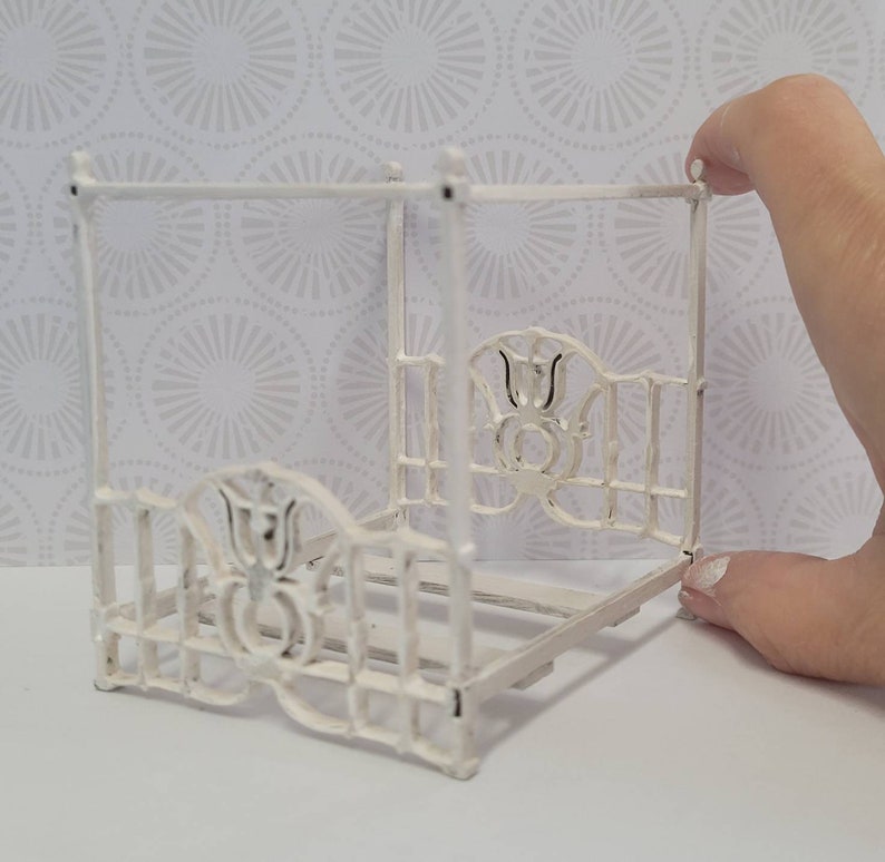Puede incluir: Marco de cama de metal blanco para casa de mu&ntilde;ecas con dosel y detalles florales decorativos.