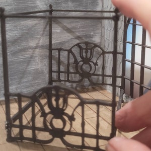 Puede incluir: Un marco de cama de metal negro con intrincados detalles de volutas. El marco est&aacute; hecho de finas barras de metal y tiene un dise&ntilde;o decorativo en la cabecera.