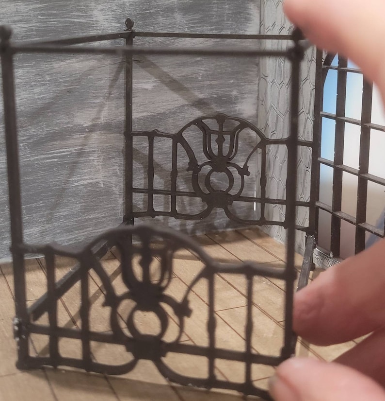 Puede incluir: Un marco de cama de metal negro con intrincados detalles de volutas. El marco est&aacute; hecho de finas barras de metal y tiene un dise&ntilde;o decorativo en la cabecera.