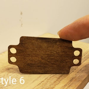 May include: A dark brown wooden tag with two holes on each side. The tag is blank and has a smooth surface. The text "Style 6" is visible below the tag.