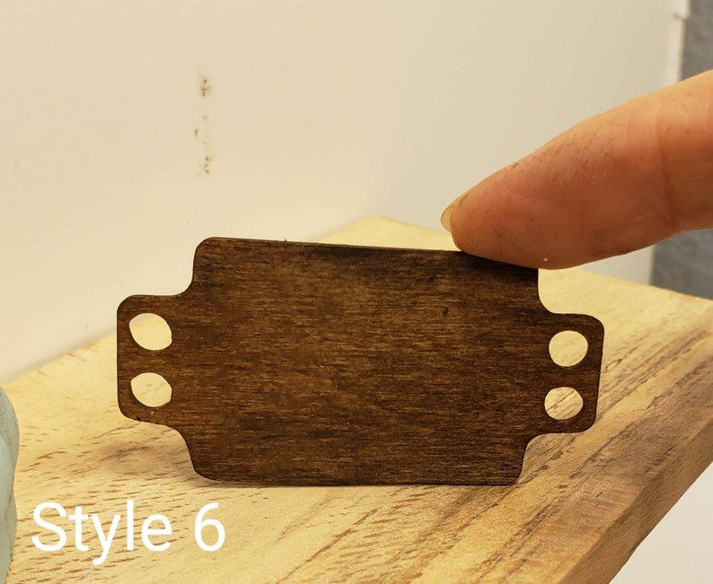 May include: A dark brown wooden tag with two holes on each side. The tag is blank and has a smooth surface. The text "Style 6" is visible below the tag.