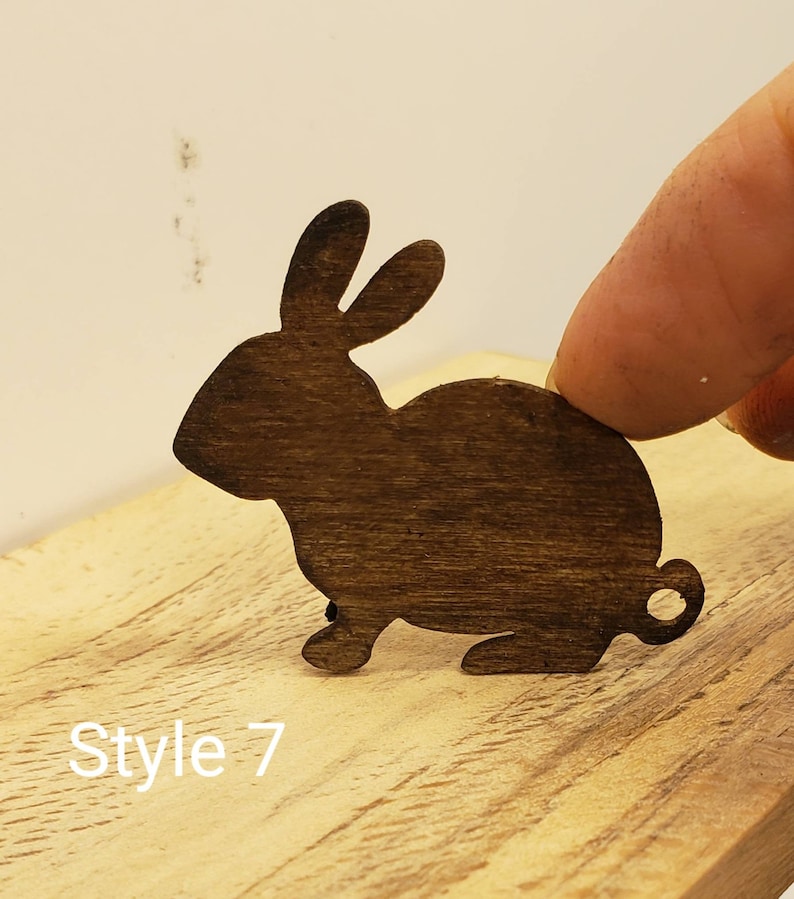 May include: A dark brown wooden rabbit cutout with a smooth, polished finish. The rabbit is in a sitting position with its ears upright. The cutout is on a light brown wooden surface. The text "Style 7" is visible in the lower left corner of the image.