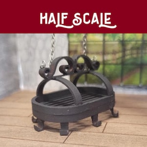 May include: A black metal hanging fireplace with a grate and decorative scrollwork. The fireplace is suspended from chains and has a half-scale label.