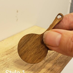 May include: A small, round, wooden cutting board with a handle. The board is stained a dark brown color. The board is labeled "Style 1".