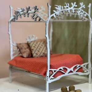 May include: A miniature white bed frame with a canopy, featuring a red dotted blanket and patterned pillows. The bed frame has a tree branch design. Two small gold boots are at the foot of the bed.