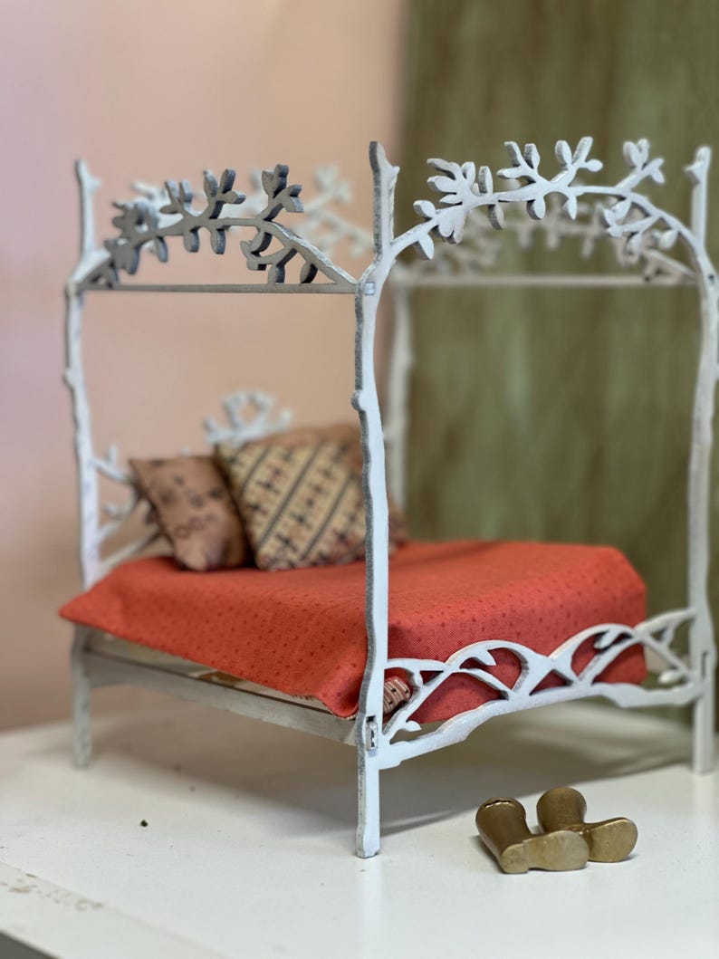 May include: A miniature white bed frame with a canopy, featuring a red dotted blanket and patterned pillows. The bed frame has a tree branch design. Two small gold boots are at the foot of the bed.