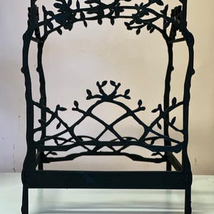 May include: A black metal bed frame with a decorative branch and leaf design. The frame has a headboard and footboard, and the top of the frame is adorned with branches and leaves. The bed frame is approximately 12 inches long and 8 inches wide.