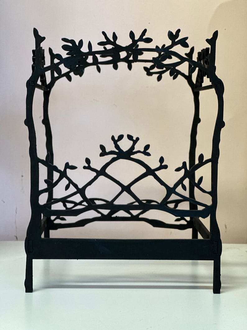 May include: A black metal bed frame with a decorative branch and leaf design. The frame has a headboard and footboard, and the top of the frame is adorned with branches and leaves. The bed frame is approximately 12 inches long and 8 inches wide.