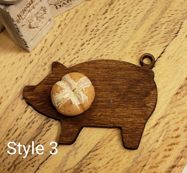 May include: A dark brown wooden pig-shaped cutting board with a round bun on top. The board has a hole in the top for hanging.  Style 3.